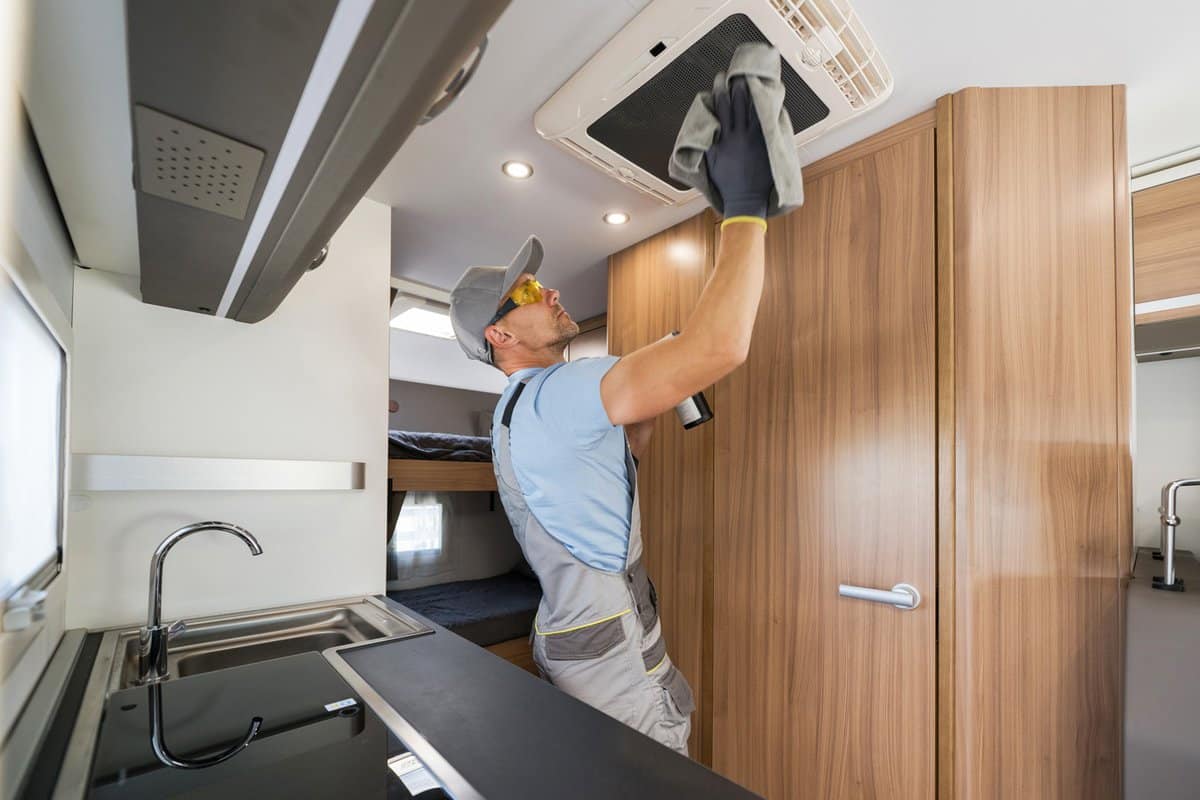 Caucasian RV Rental Company Worker in His 40s Cleaning Motorhome Ceiling Mounted Air Condition Unit. Preparing Camper Van RV For the Season.