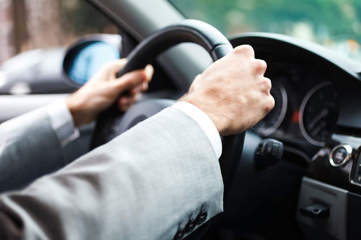 Man in a suit driving a car with the hand on a in the steering wheel