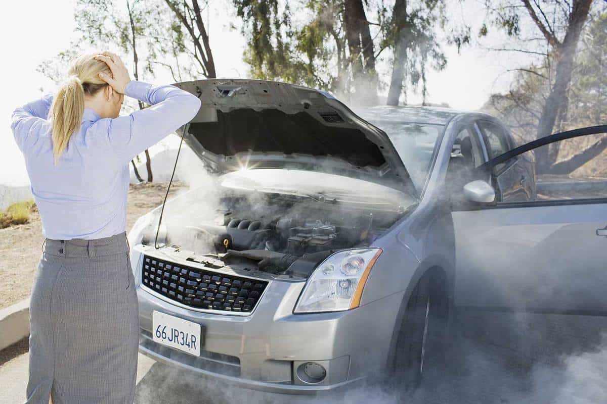 Frustrated woman looking at smoking car engine