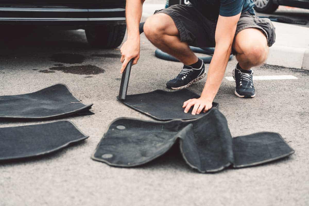 Man using vacuum to clean car floor mats