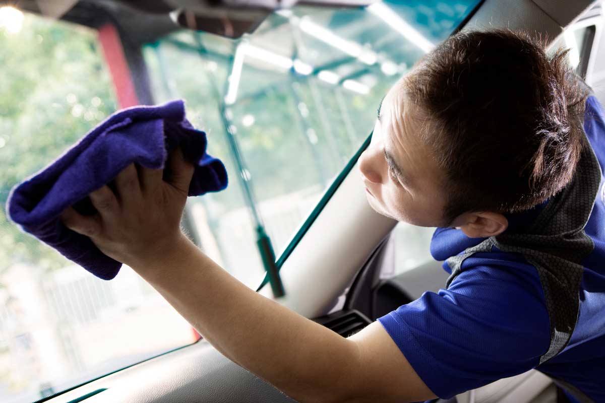 A man cleaning the inside of the windshield using microfiber cloth