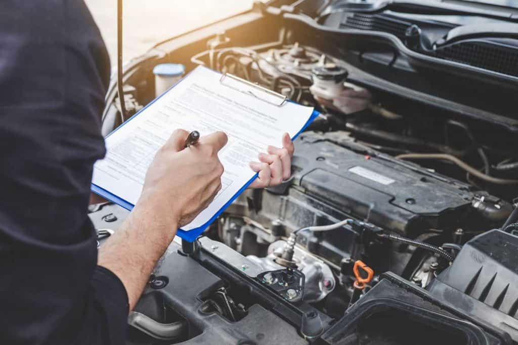 Automobile mechanic checking a car engine with inspecting and writing checklist for repair, car service and maintenance