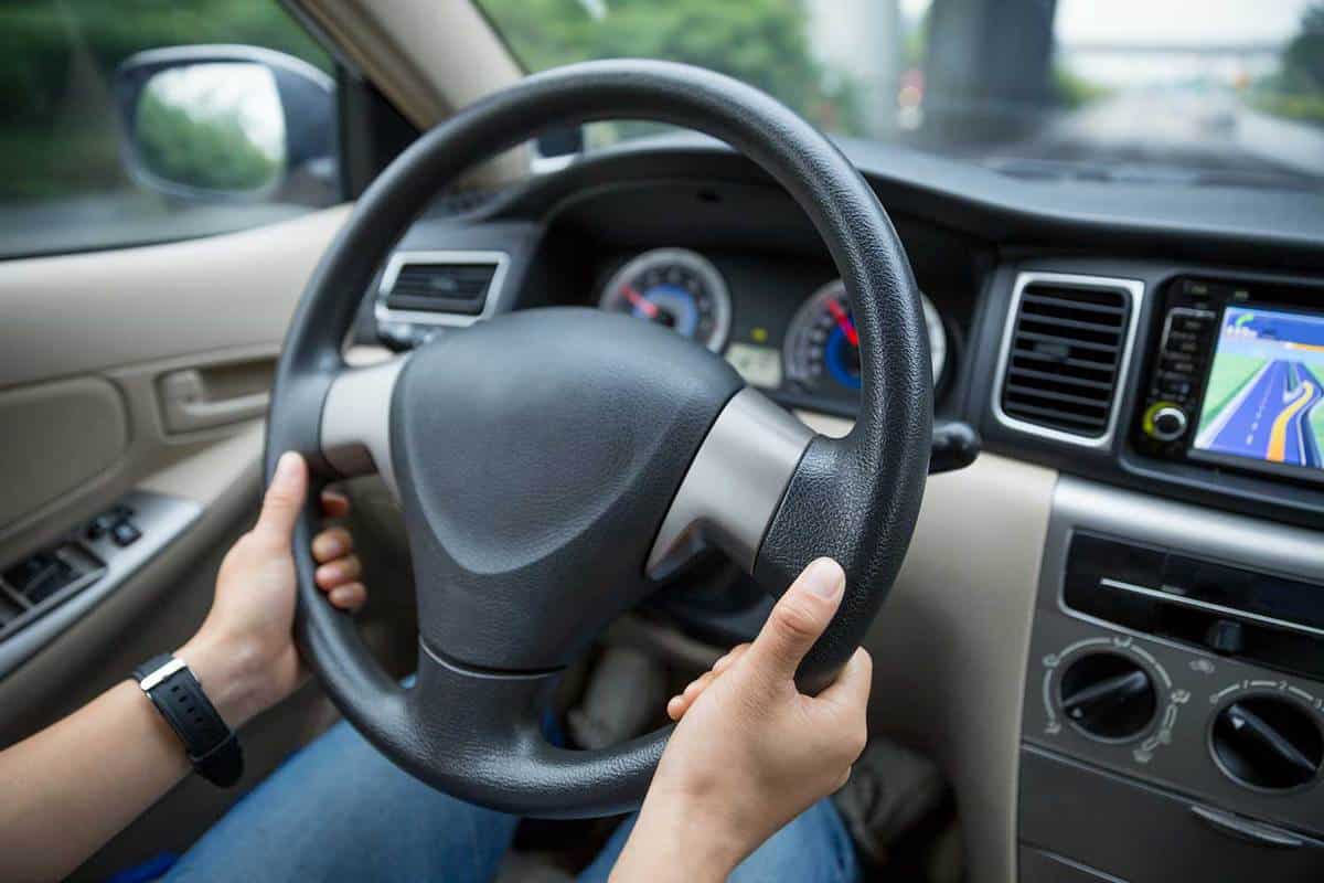 Hands holding steering wheel while driving car on city road