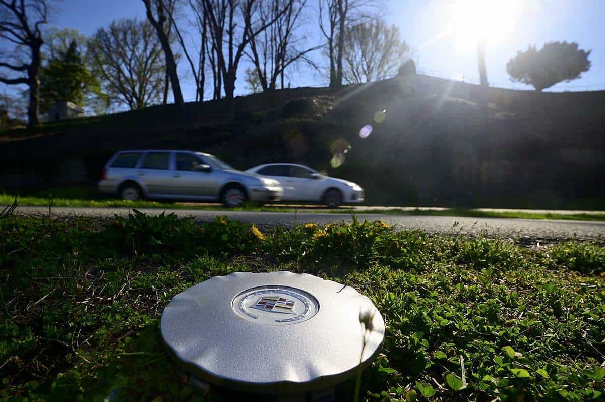 Hubcap left on side of road, with grey SUV and white car on the background