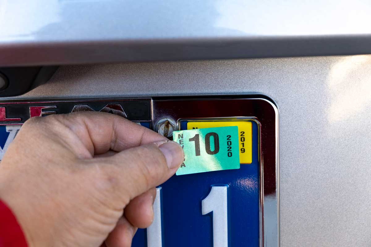 Man placing 2020 sticker into license plate, What Are Car Tags [And What To Do When They Expire]