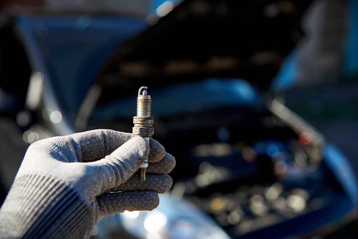 Spark plug for engine in male hand on the background of a car with an open hood