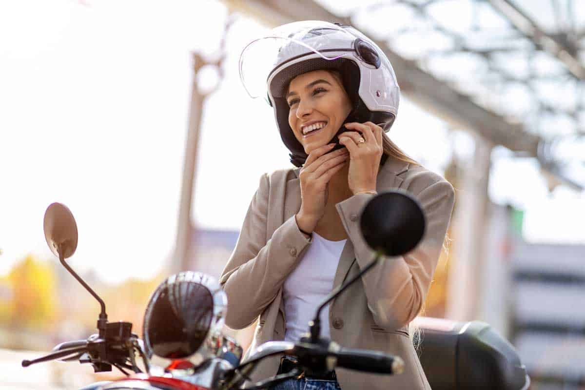 Woman riding motorcycle and putting on helmet, 12 Gorgeous Women's Motorcycle Half Helmets (Inc. With Visor)