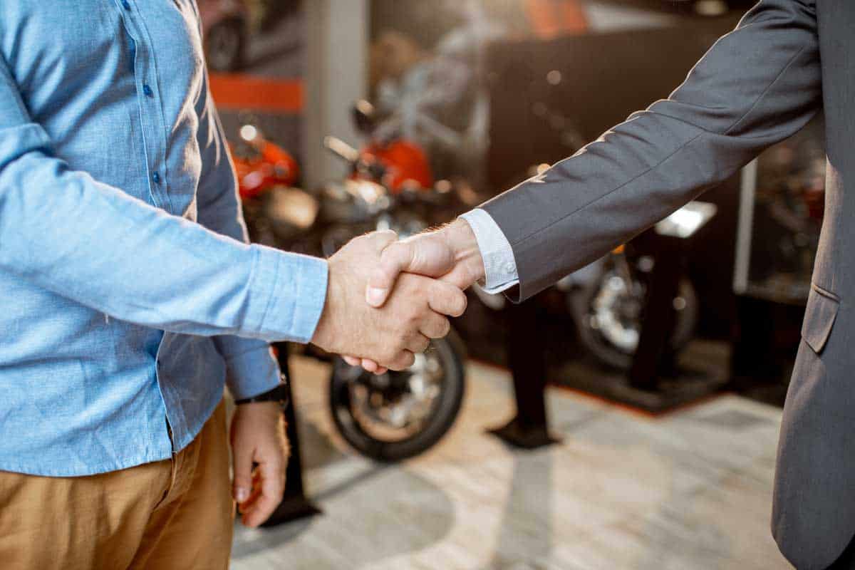 Client shaking hands with a salesman having deal in the showroom with sports motorcycles, close-up