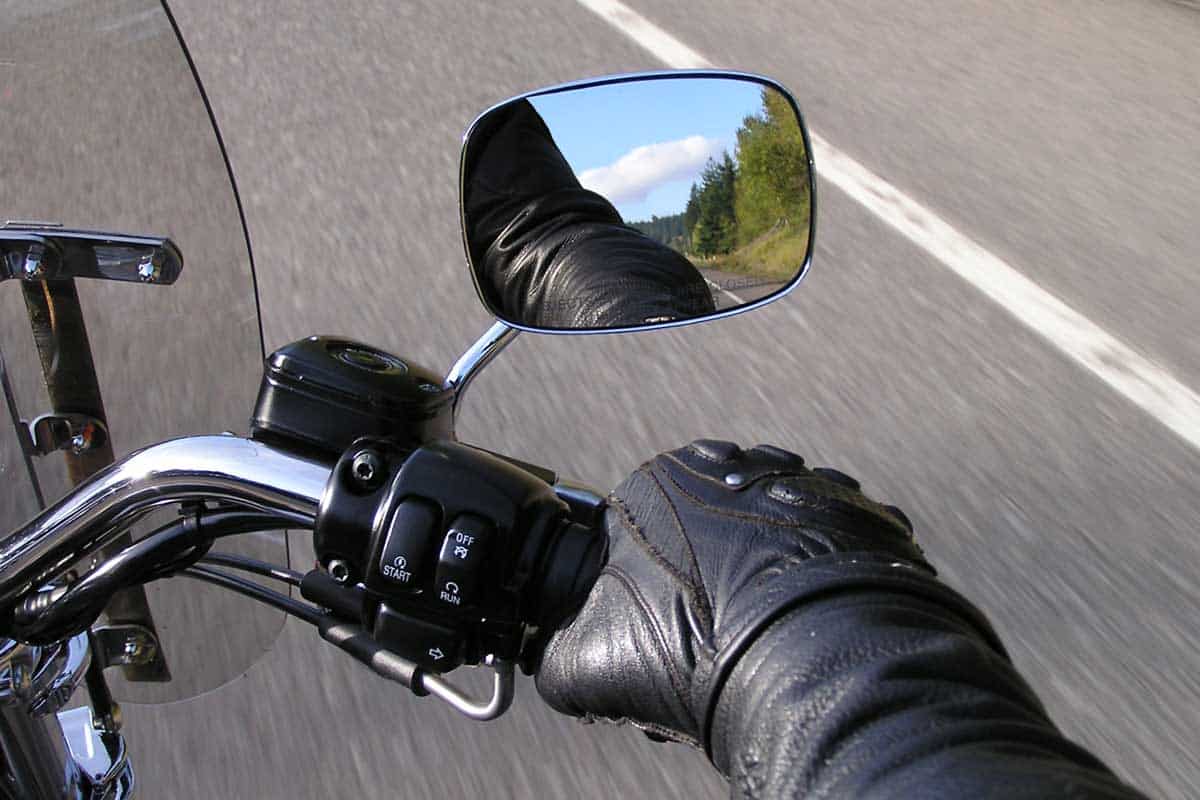 Motorcyclist's hand on throttle with visible beautiful blue sky and greenery in motorcycle side-mirror, Do Motorcycles Need Mirrors?