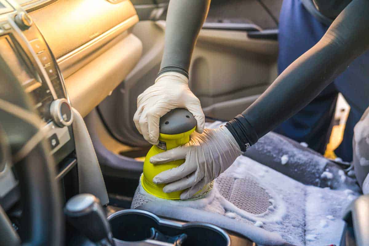 a man cleaning car interior by use foam chemical and scrubbing machine.