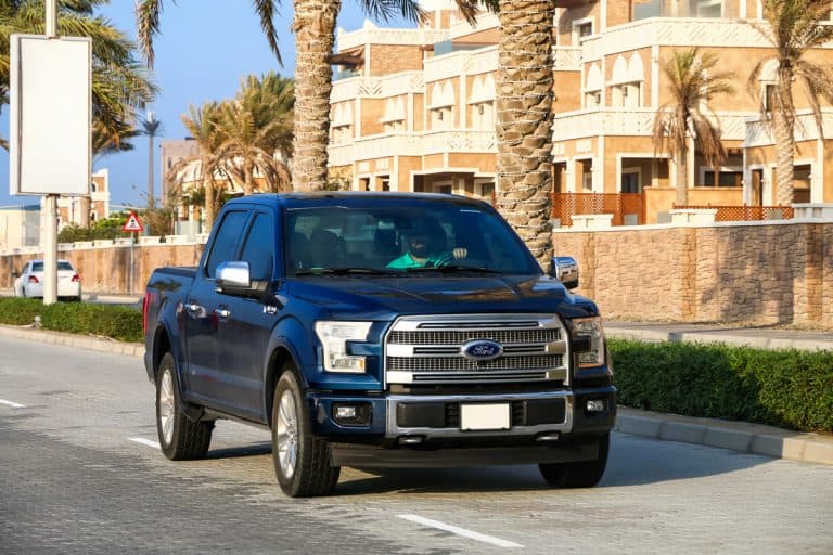 A dark blue colored Ford F-150 moving down the road with a person driving it, Ford Regular Tow Package vs Max Tow Package - What Truck Owners Need To Know