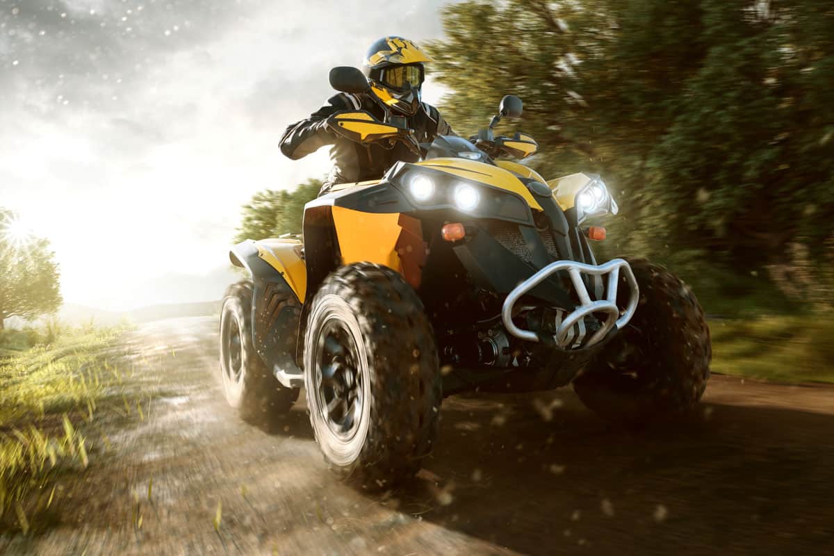 A rider driving the atv with headlight on going through the forest