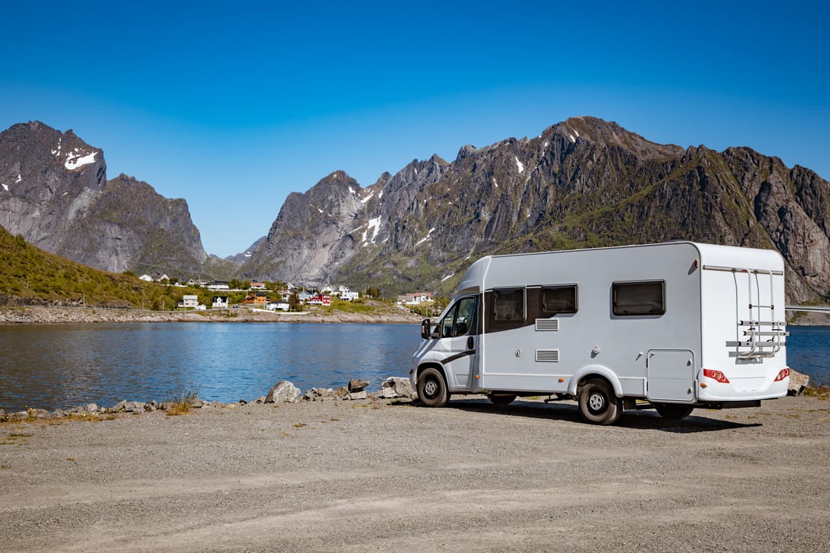 A travel RV parked near a lake with an awesome panoramic mountain range view, What Does Shore Power Mean in an RV?