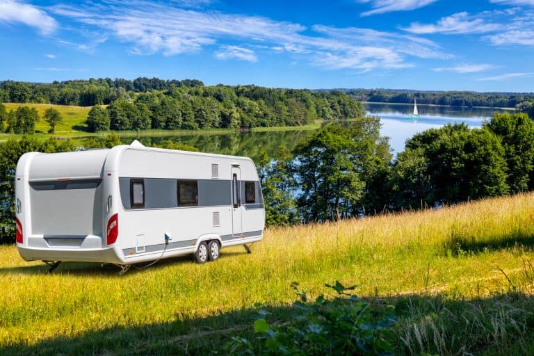 A travel trailer parked on a grassy field with an overview of a lake, How Much Does A 25′ Travel Trailer Weigh? [Inc. 16 examples]