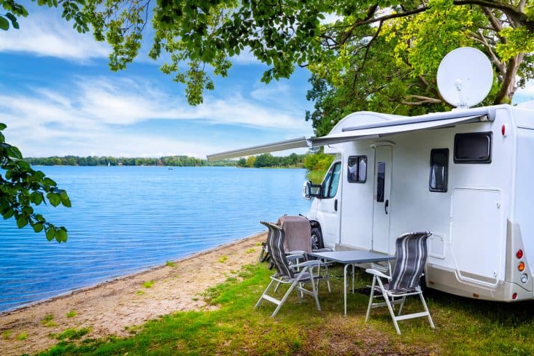 An RV parked on the side of the lake next to a tree for shade, How Much Does RV Camping Cost? [A detailed Analysis with Examples]