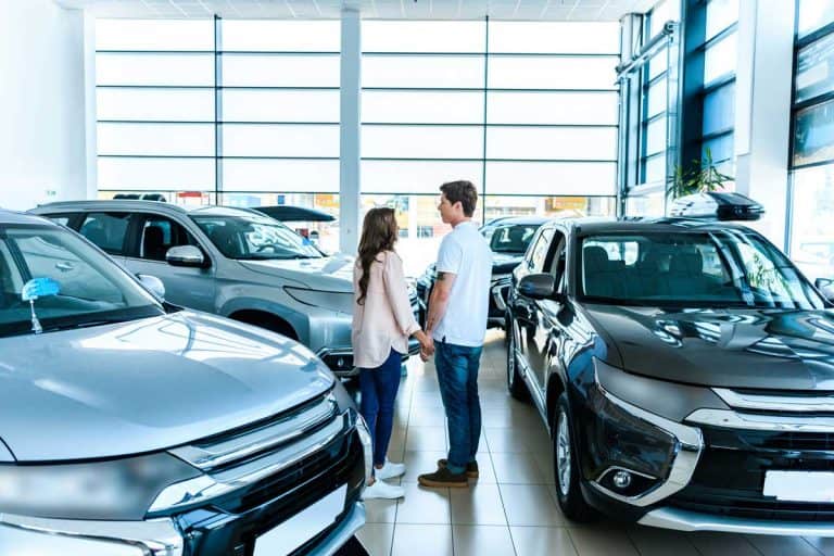 Couple standing face to face in showroom, Do Dealerships Register Cars for You? [and How Long It Can Take]