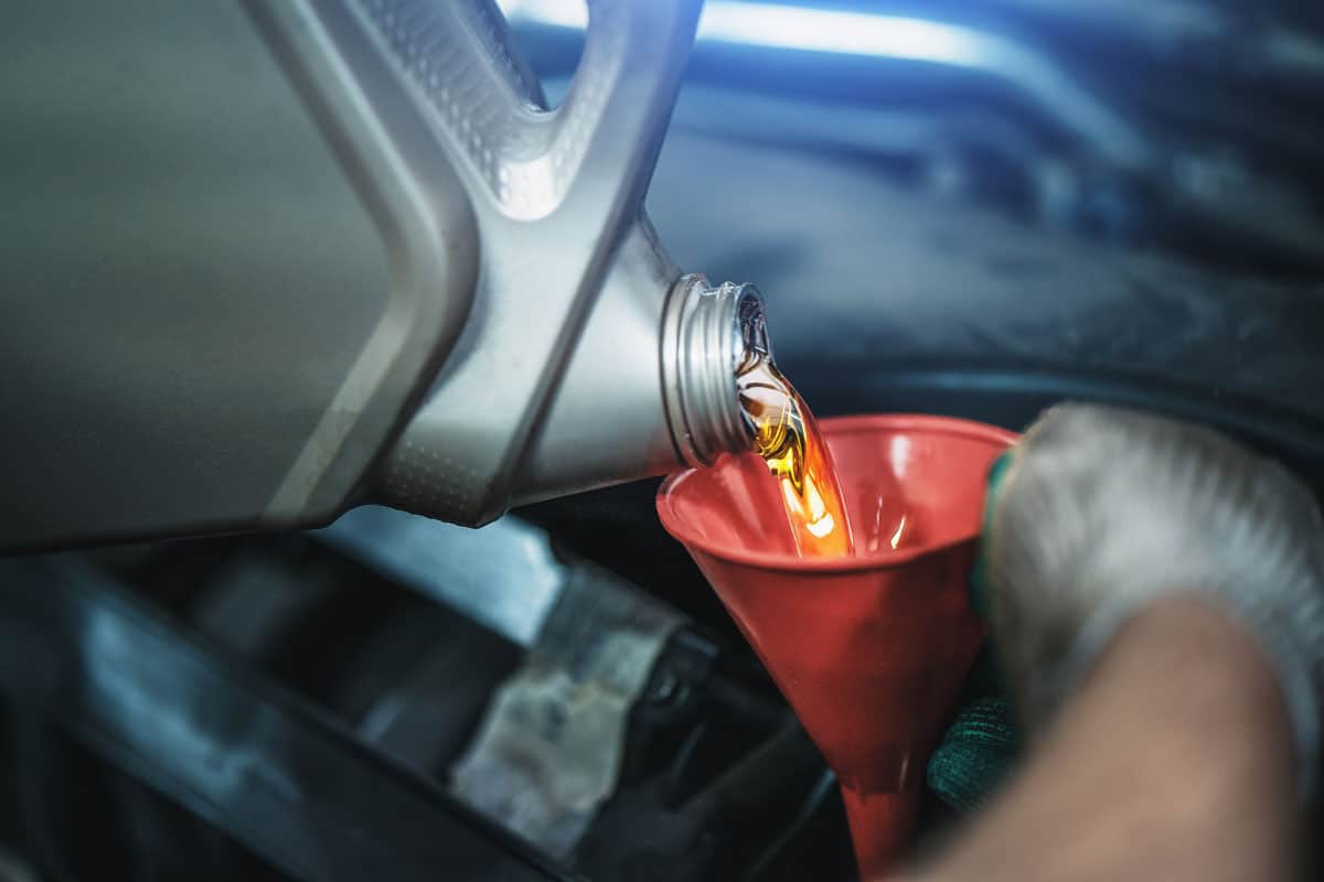 Worker pours new synthetic motor oil from canister into funnel at car service