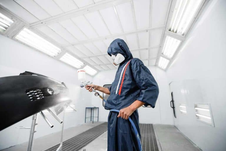 worker painting a car black blank parts in special garage, wearing costume and protective gear, How Much Does it Cost to Repaint a Car? [Touch Ups vs. Full Paint Job)