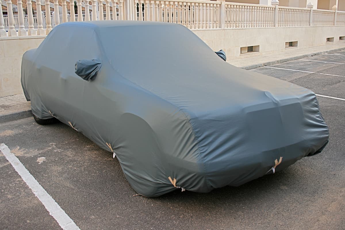 A car with a heat proof cover parked on the side of the street, Do Car Covers Damage Your Car? [Inc. 4 Things You Can Do To Prevent Damage]