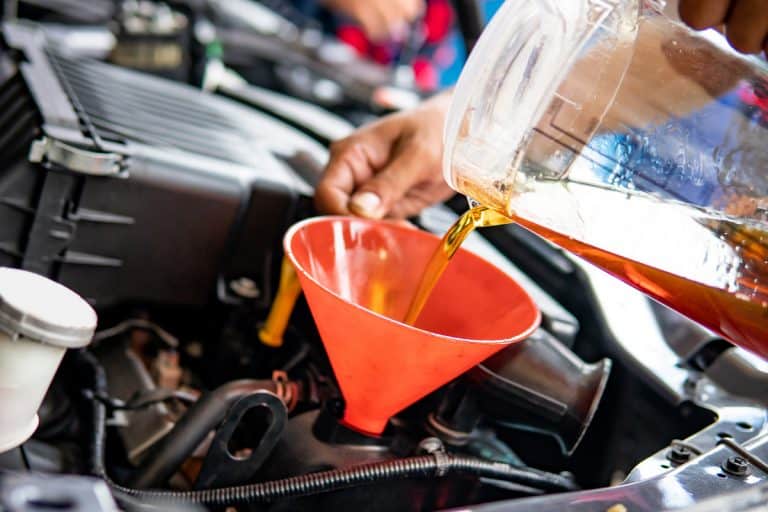 A mechanic pouring oil into the engine of a car, 5 Best Engine Oil Additives For Reducing Engine Noise