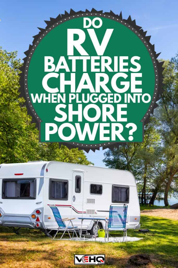 A travel trailer with chairs set up for camping and parked near a lake with a scenic view, Do RV Batteries Charge When Plugged Into Shore Power?