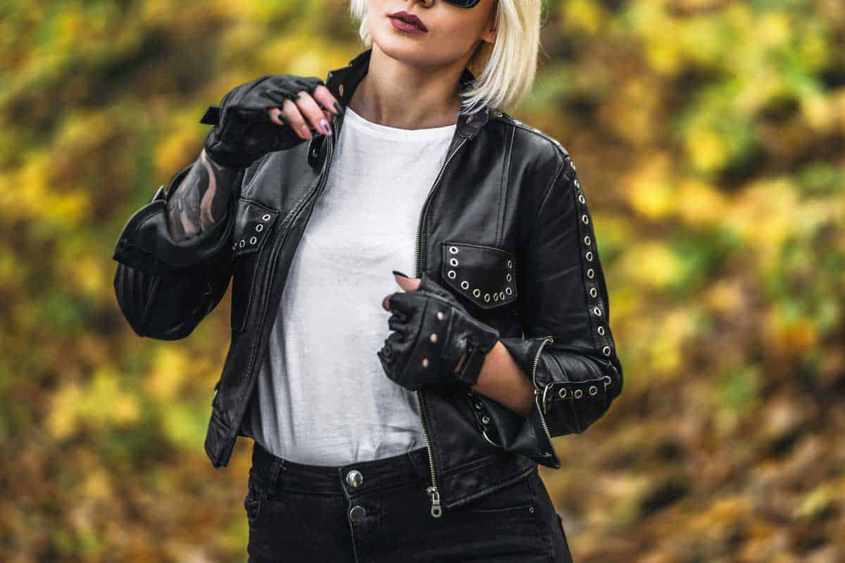 Pretty blonde biker styled women in black leather jacket with sunglasses standing outdoors in the forest with colorful blurred background, Can You Dry Clean Motorcycle Leathers?