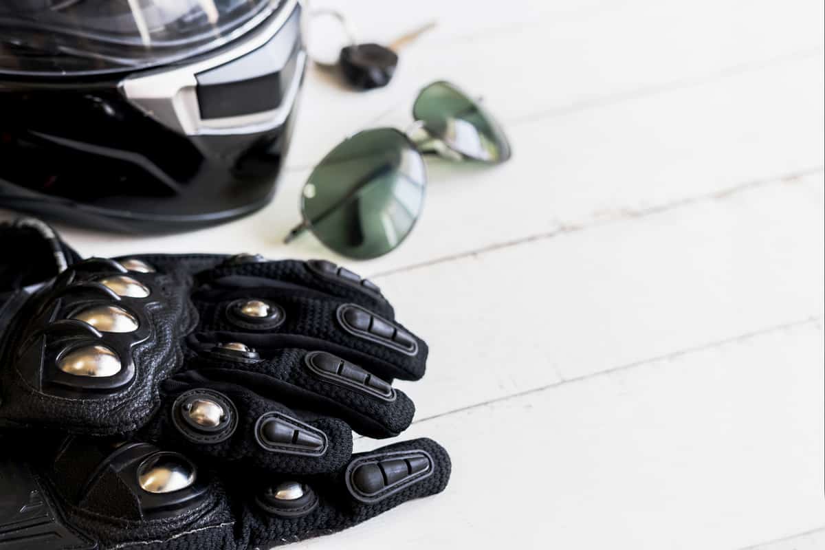 A black motorcycle glove with metal plated knuckles and a helmet on the table, How To Wash Motorcycle Gloves? [3 Steps]