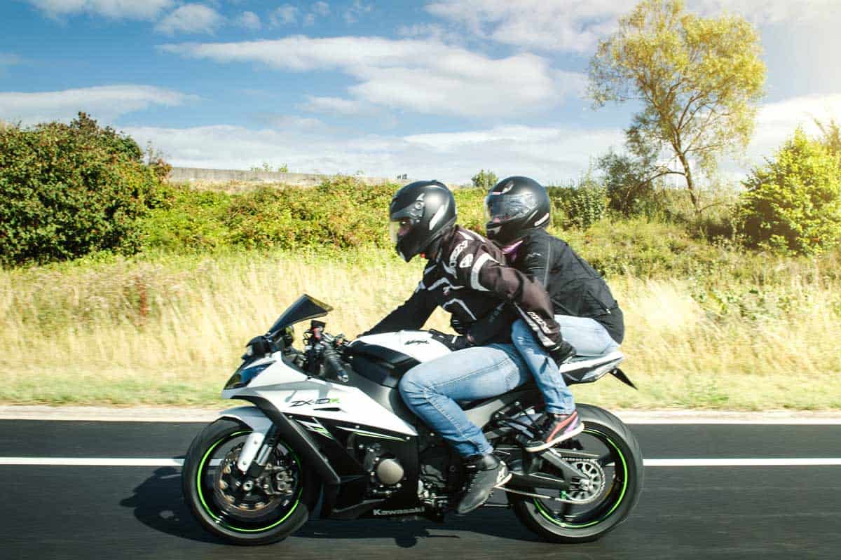 Side view of couple driving fast on highway on their supercharged motorcycle, What To Wear As Motorcycle Passenger? [6 Items You Should Seriously Consider]