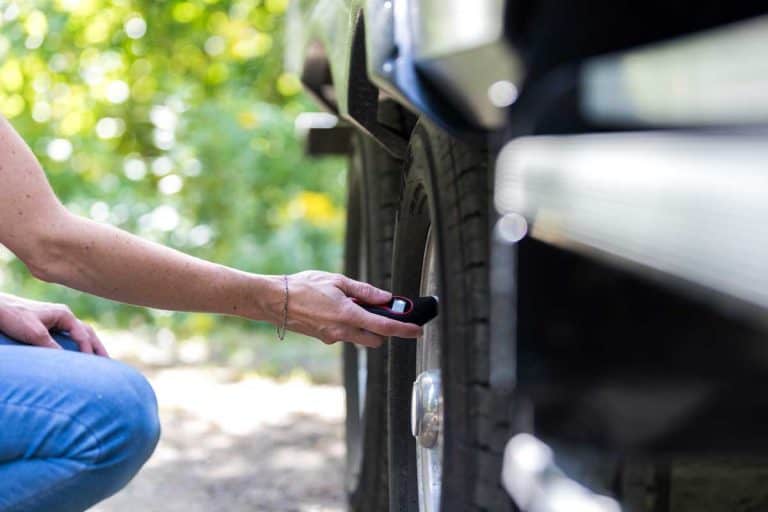 A woman is verifying the tire pressure of her camper trailer before leaving campground, How To Inflate Travel Trailer Tires? [5 Steps]
