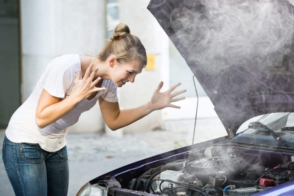 Frustrated young woman looking at broken down car engine on street