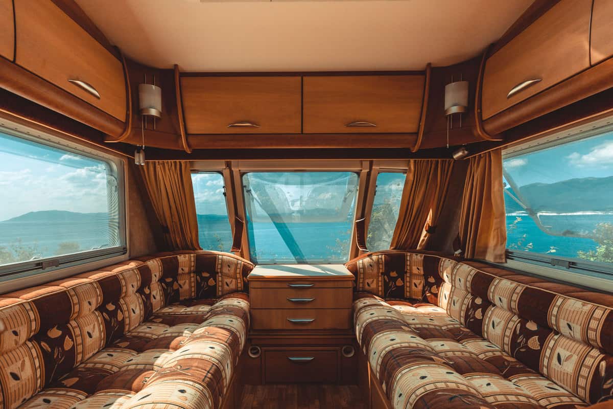 Interior of a rustic themed caravan with long sofas, a center table, and overhead cabinets with overlooking windows, How To Seal RV Windows To Stop Leaks