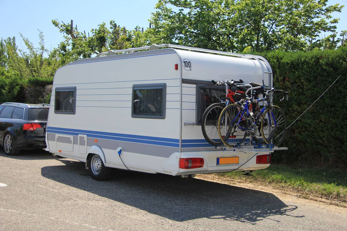 An SUV towing a camper trailer with mountain bikes clamped on the back of the camper, Do Camper Outlets Work On Battery?