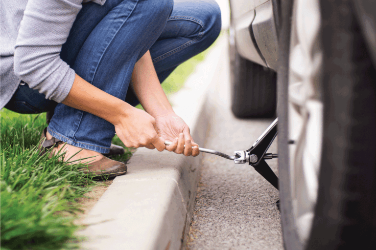 Closeup of unrecognizable woman changing flat tire on her car. She's kneeling on the roadside next to rear left wheel and lifting car jack. What SUVs Have Full-Size Spare Tires