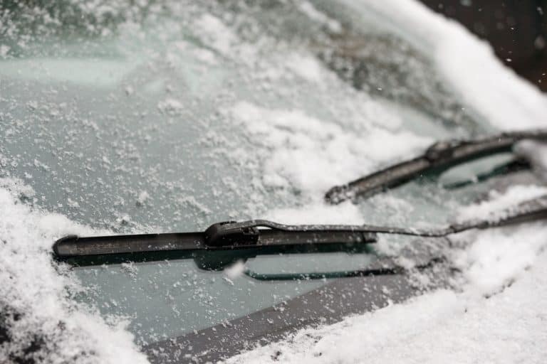 Car wiper blades clean snow from car windows. Flakes of snow covered the car with a thick layer