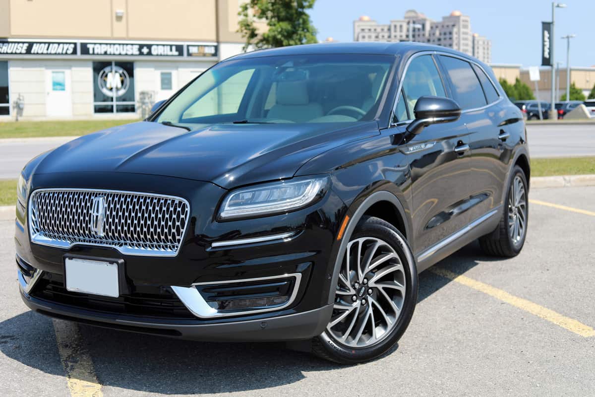 Front and side view of a brand new shiny Lincoln Nautilus 2019 Reserve model with premium 20 inch wheels in black color on an outdoor parking lot.