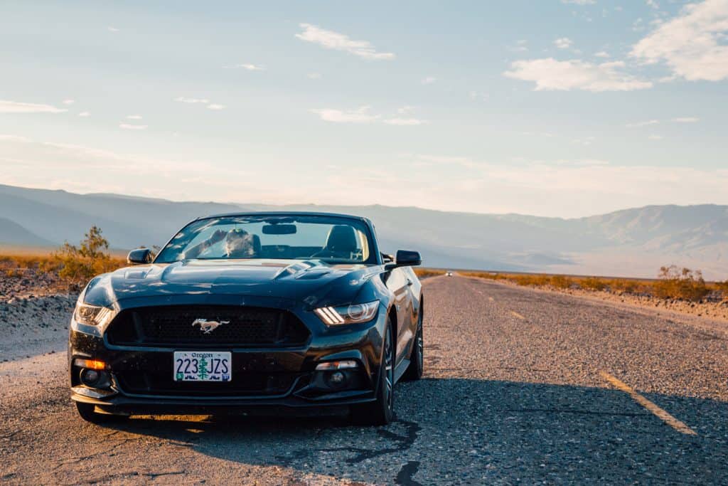 Black Ford Mustang GT convertible is parked by the infinite long road in the middle of a death valley in Nevada, USA