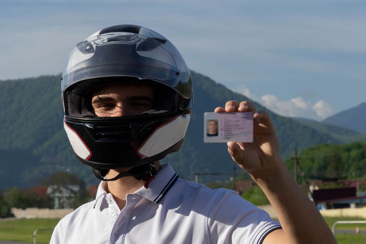 Young man in a helmet on the motorbike is showing driving license, How To Get A Motorcycle License In California?