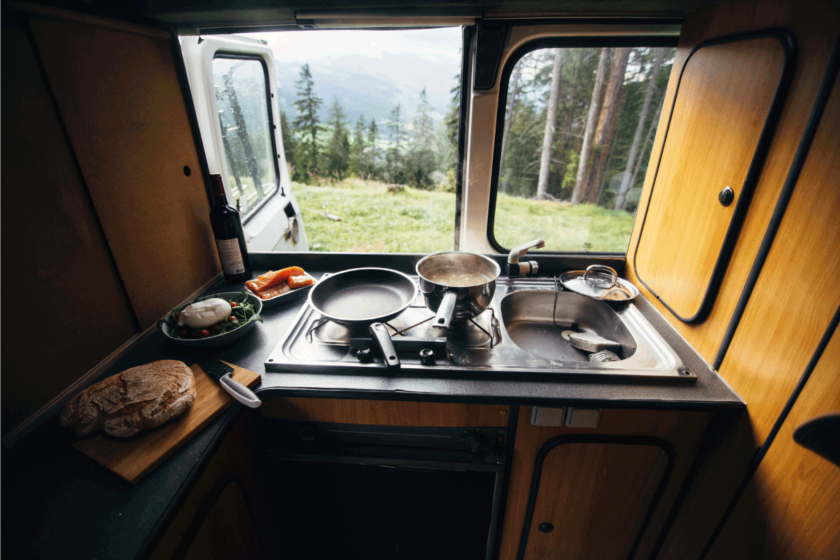 Interior of travel camping van or camper RV with stove and sink. Vanlife lifestyle vibes, cooking on campsite during road trip with amazing view of mountains. 11 Awesome RV Kitchen Ideas