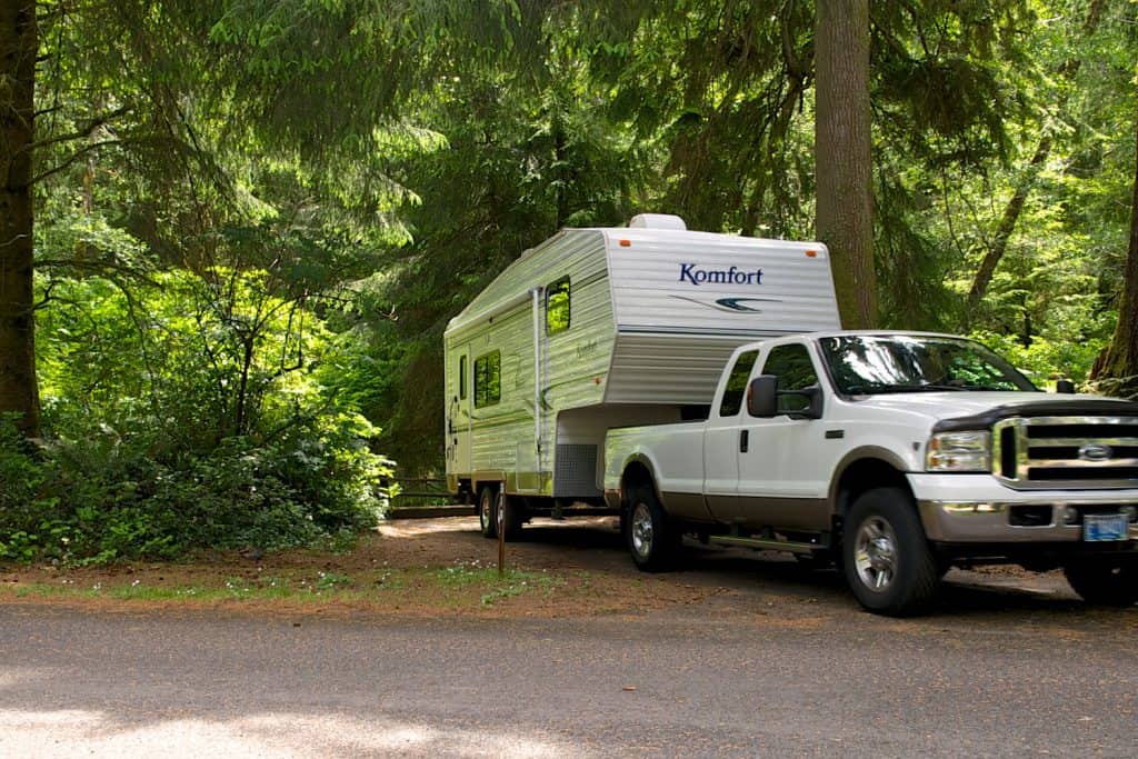 A Komfort brand Fifth Wheel Travel Trailer and Ford F350 Pickup are shown pulling out of the camping space, Can An F350 Pull A Fifth Wheel?