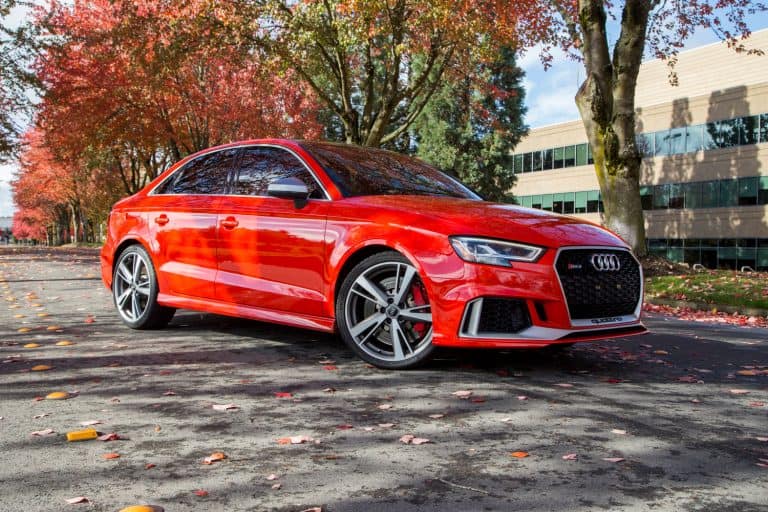 A red Audi RS3 luxury sports car is parked on a road covered with foliage leaves on a sunny fall day, Do Audi Cars Need Premium Gas? [Breakdown By Model]