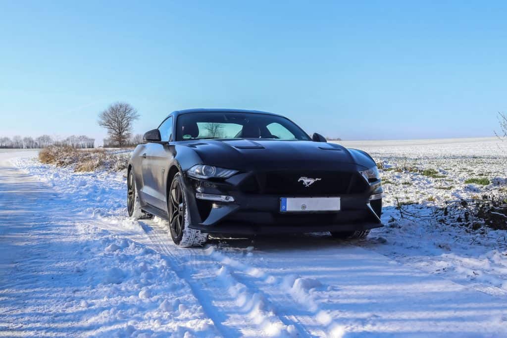 Black ford mustang sports car in front of a winter landscape in Germany on a sunny day, Is The Ford Mustang Rear Wheel Drive Or AWD?