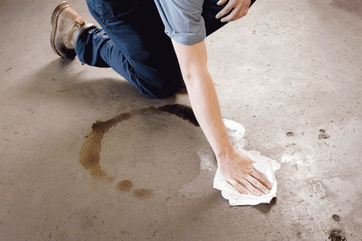 Oil clean-up in a workshop. A man cleaning-up an oil spill on a workshop floor. The man is wearing work boots and mechanic's clothing.