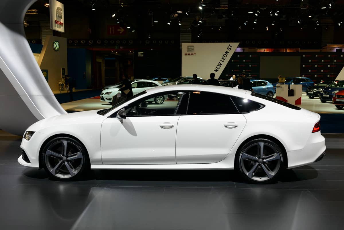  White Audi RS7 Sportback four door executive car on display at the Brussels motor show. People in the background are looking at the cars.