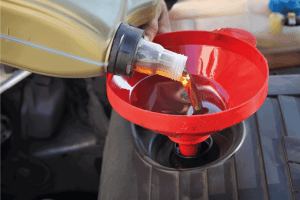 man filling engine oil from a container to a funnel on the engine. What's the Best Oil for Buick Encore [And How Often to Change It]