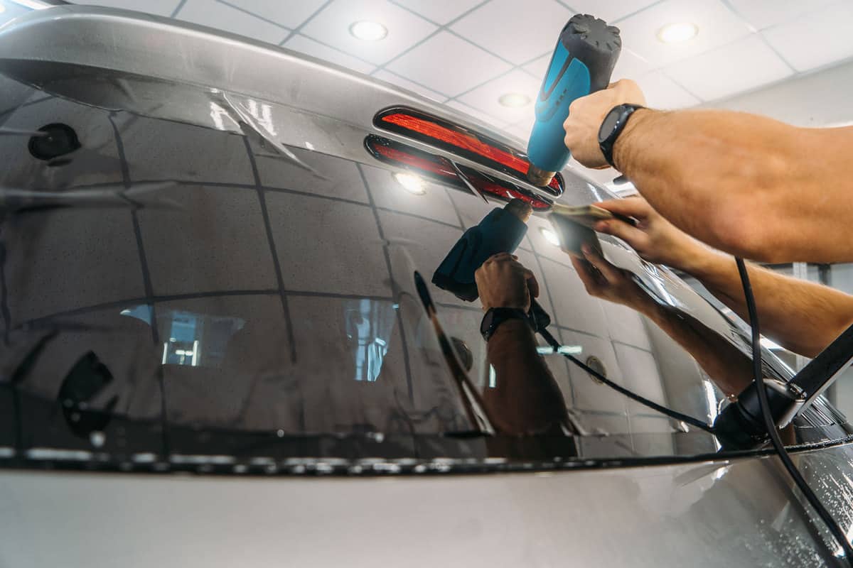 A worker doing some detailing work on the back windshield of the car, Do Car Dealerships Detail Cars? [With Other Pertinent Info!]