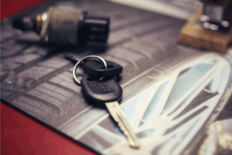 Close up image of a pair of keys with a spark plug in the background on a counter in a auto repair shop. Should A Car Be Sold With 2 Keys [Including A Used Car]