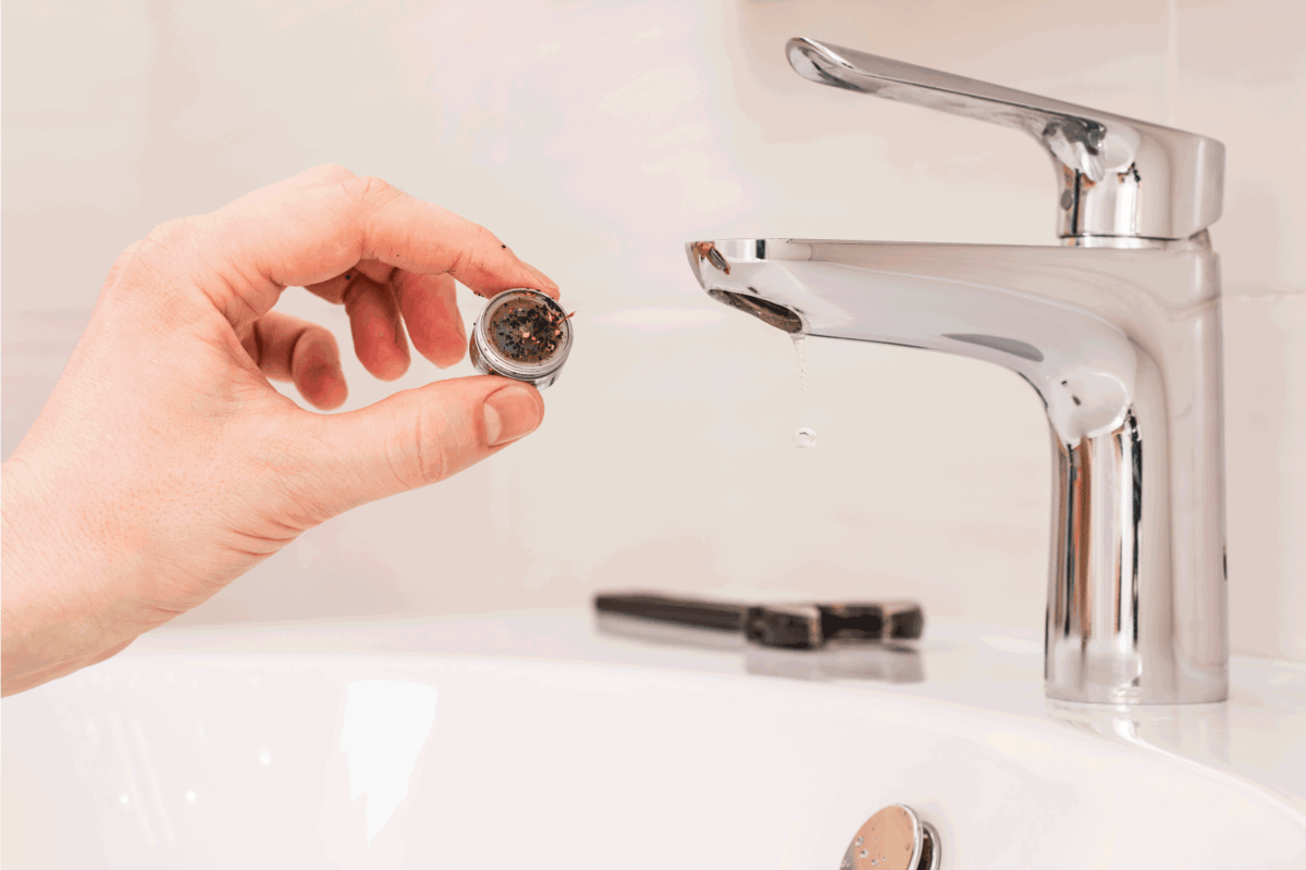 Faucet cleaning. Person's hand holds a clogged aerator. Sediment in water