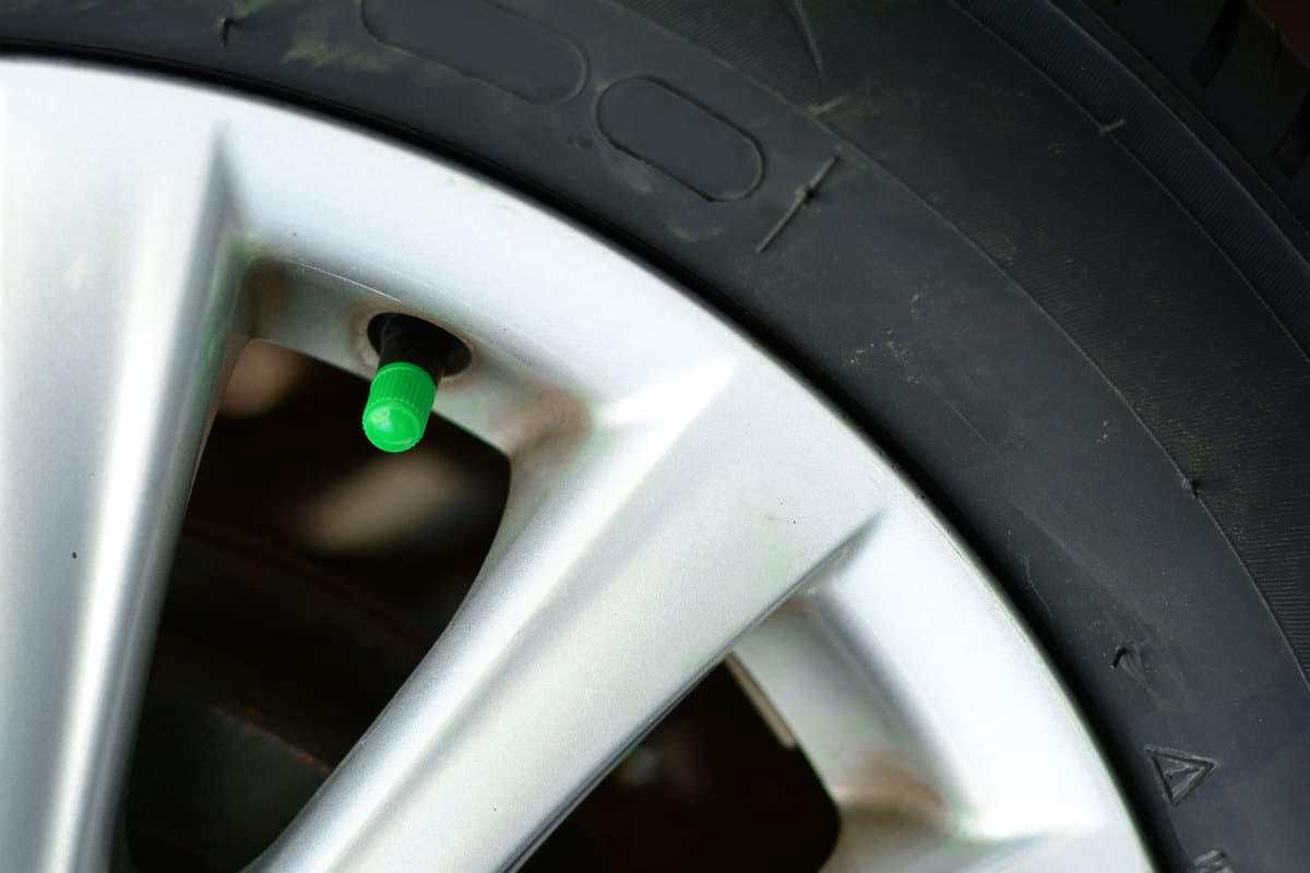 The green cover of tyre pressure valve on metal wheel with black tyre