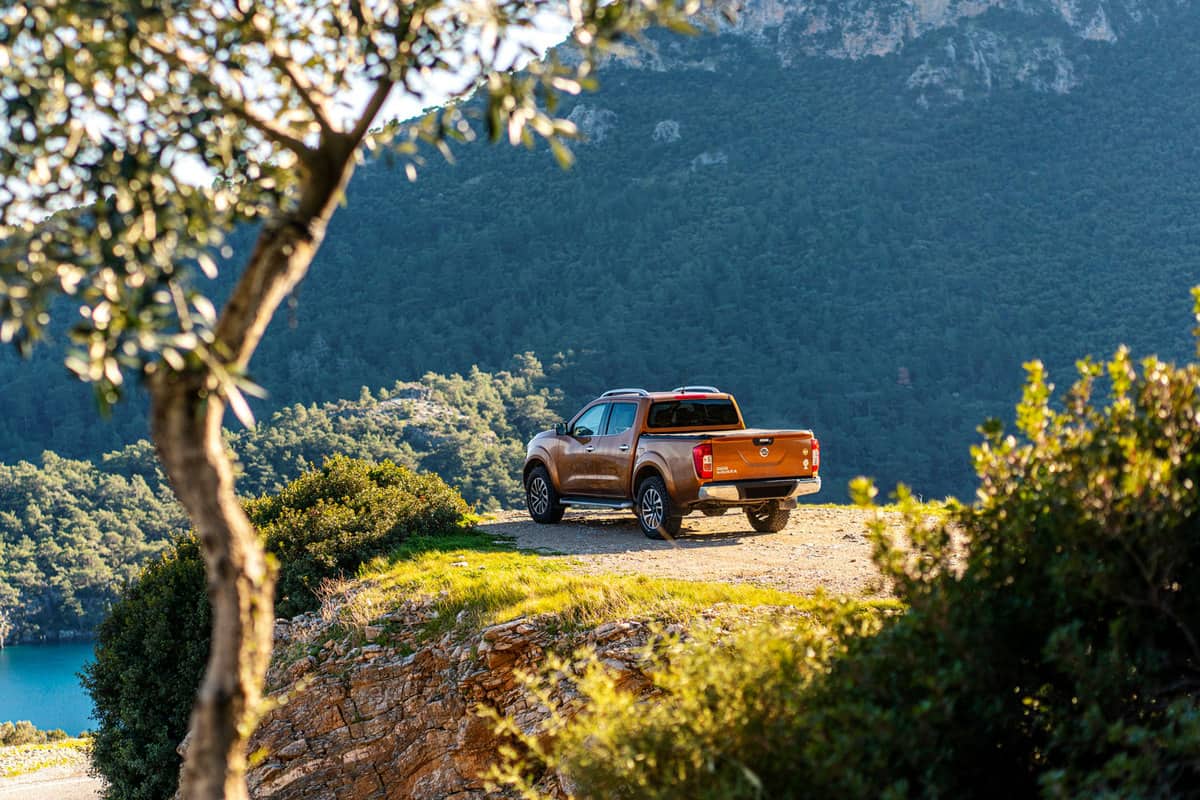 A brown Nissan Frontier parked near a cliff overviewing a gorgeous panoramic view of the mountains and landscape, Nissan Frontier: NISMO Package Vs LE
