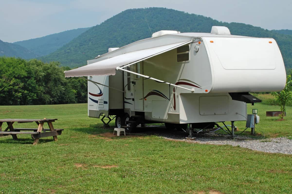 A fifth wheel trailer rv camping in front of a mountain range with the awning extended